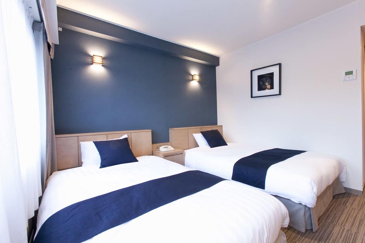 Habitación de hotel con dos camas, una mesita de noche con teléfono y dos lámparas de pared.