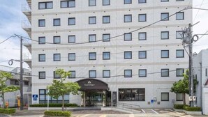 Un hotel de varios pisos con fachada uniforme, una entrada central y un estacionamiento al frente.