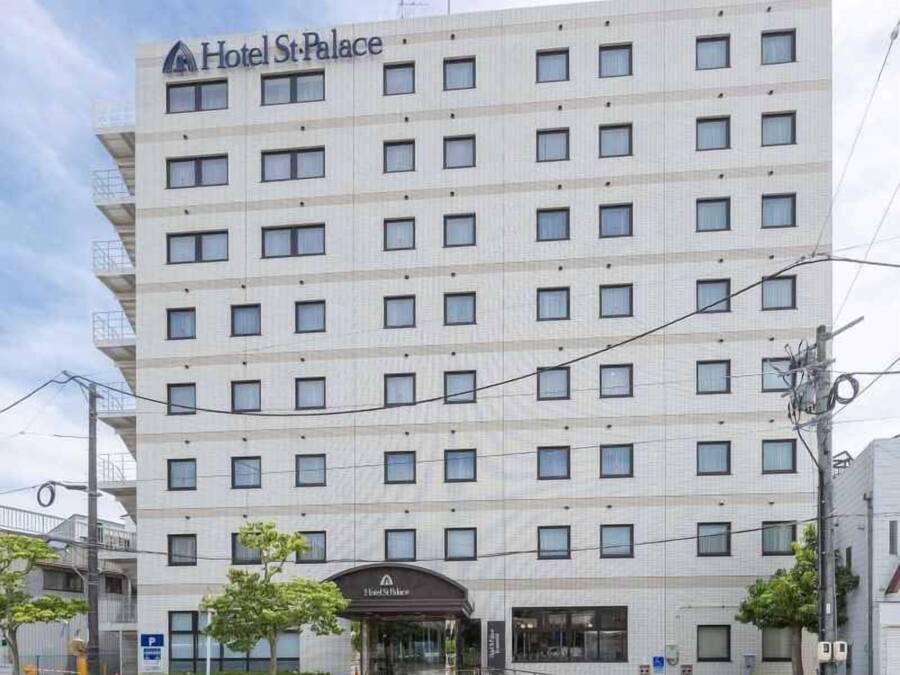 Un hotel de varios pisos con fachada uniforme, una entrada central y un estacionamiento al frente.