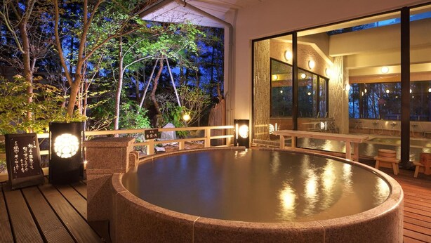 Zona de baño termal con terraza de madera, paredes de piedra y asientos.