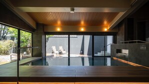 Una piscina interior moderna con techo de madera, paredes de vidrio y vistas al exterior.