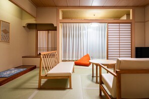 Ett traditionellt japanskt rum med tatamimattor på golvet, en låg träbänk, en bekväm soffa och ett litet bord.
