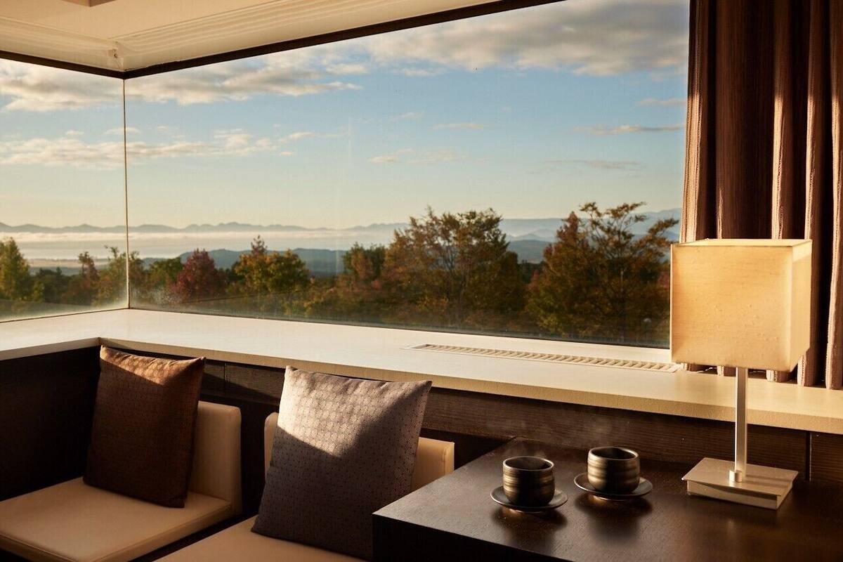 Ein Zimmer mit einem großen Fenster, einer Couch, einem Tisch mit zwei Tassen und einer Lampe.