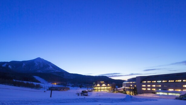 A snow-covered landscape with a mountain in the background and a building with illuminated windows. - Hoshino Resorts Bandaisan Onsen Hotel (Bandai)