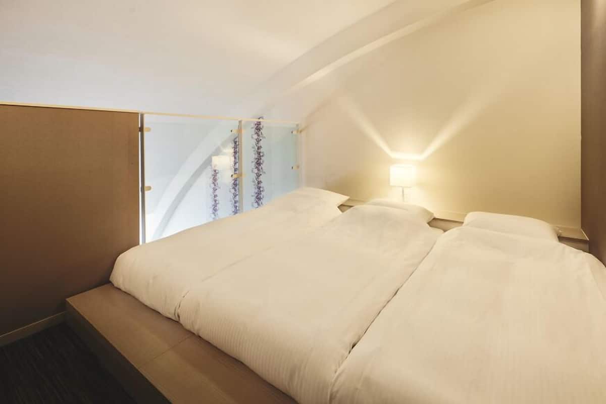 Ein Hotelzimmer mit Bett, Nachttisch, Lampe und einem Fenster mit Vorhängen.