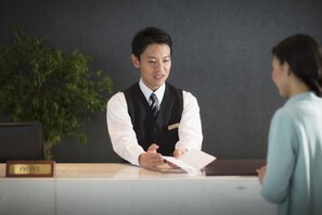 A hotel reception desk with a nameplate, a plant, and a computer monitor. - Hoshino Resorts Bandaisan Onsen Hotel (Bandai)
