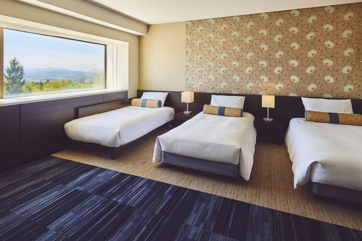 Quarto de hotel com duas camas de solteiro, uma janela grande com vista e parede com padrão.