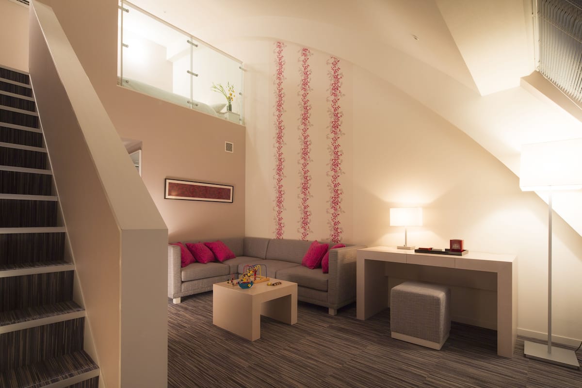 Ein modernes Wohnzimmer mit Treppe, einer Couch, einem Couchtisch und einem Schreibtisch mit Lampe.