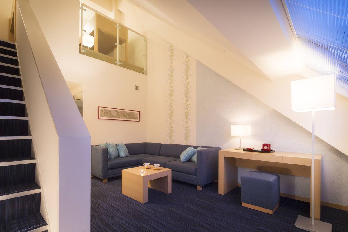 Ein modernes Hotelzimmer mit Treppe, Sofa, Couchtisch, Schreibtisch und Lampe.