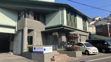 Un hotel con fachada moderna, entrada protegida por un portón y un estacionamiento con coches.