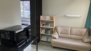 Una habitación con un microondas negro sobre una mesa negra, un sofá beige y una estantería con diversos objetos.