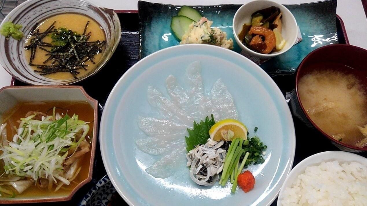 A table with various dishes including a bowl of soup, a plate with sashimi, and other food items.