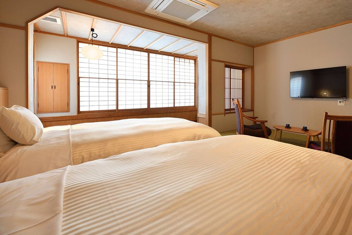A hotel room with two beds, a TV, a desk, and a window with a view.