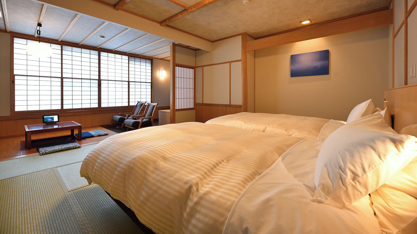 A traditional Japanese-style bedroom with tatami flooring, a large bed with white bedding, a television on a low table, and sliding doors.