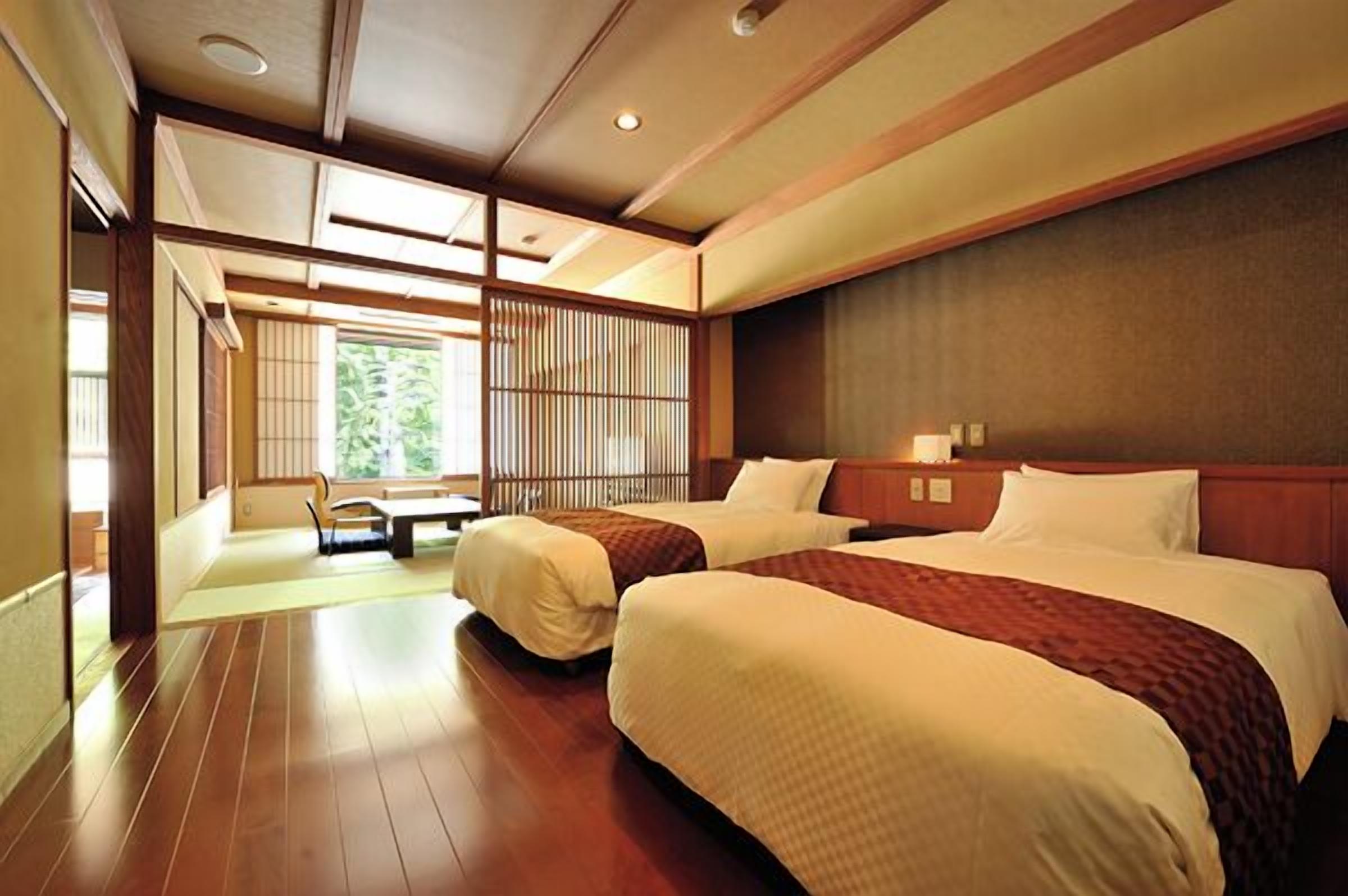 A hotel room with two beds, a wooden floor, a view of greenery, and a traditional Japanese sliding door.