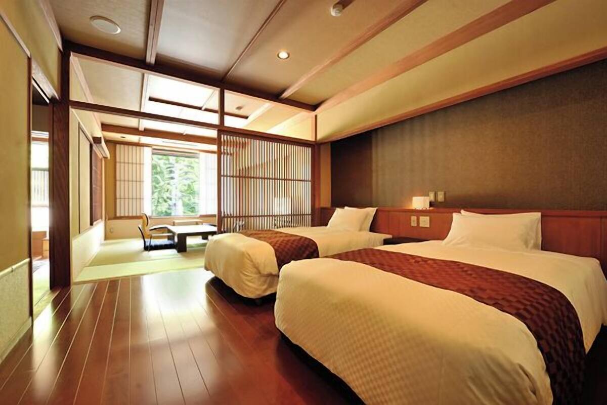 A hotel room with two beds, a wooden floor, a view of greenery, and a traditional Japanese sliding door.