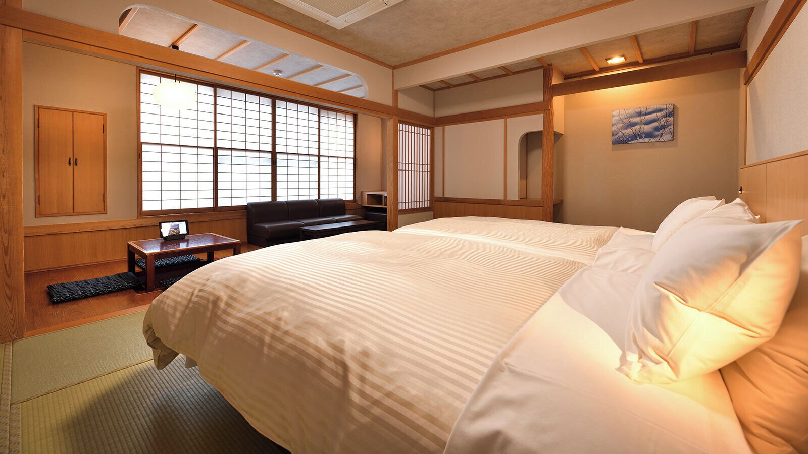A traditional Japanese-style bedroom with tatami flooring, a large bed with white bedding, a wooden desk, and a sliding shoji screen window.