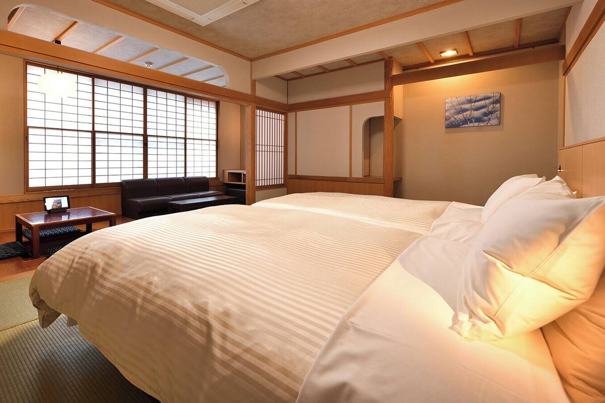 A traditional Japanese-style bedroom with tatami flooring, a large bed with white bedding, a wooden desk, and a sliding shoji screen window.