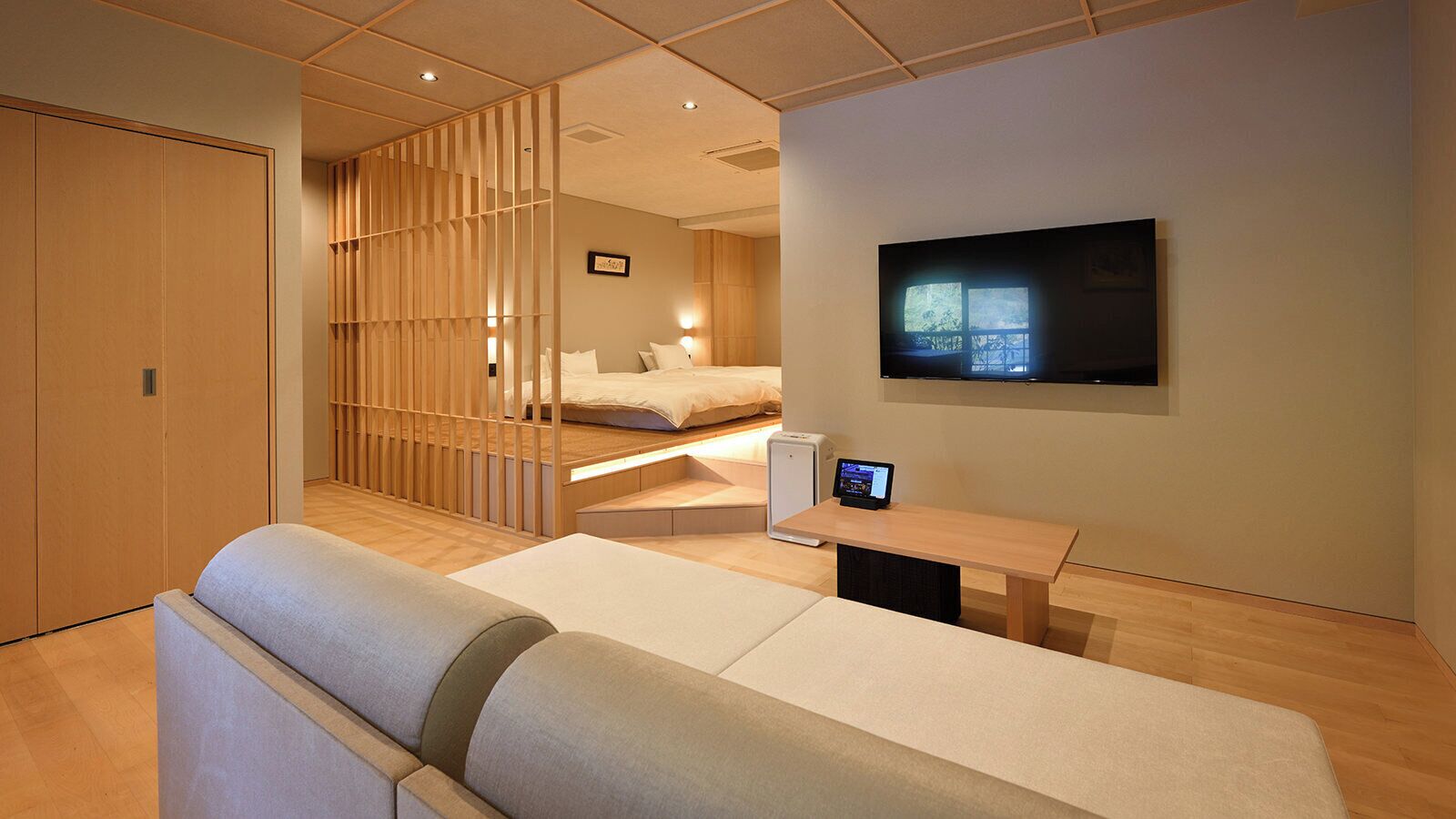 A modern hotel room with a sofa, a bed, a TV, and a desk with a laptop.