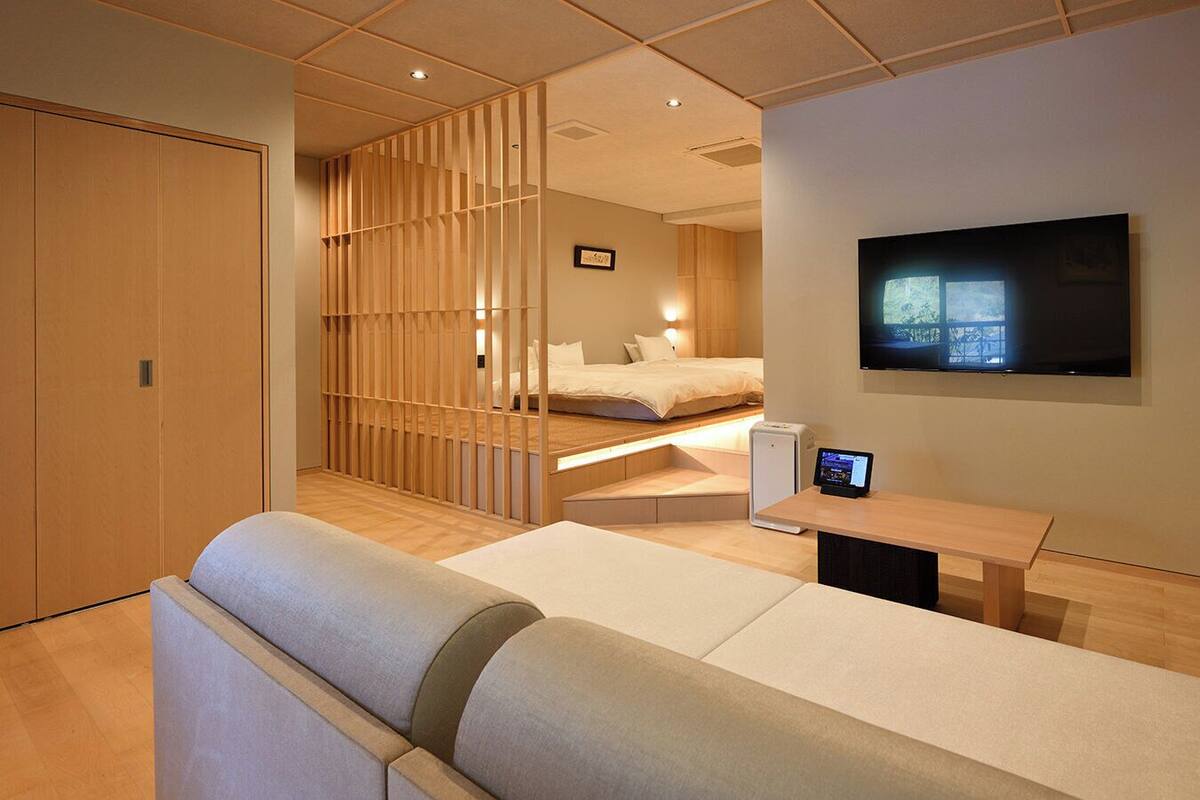 A modern hotel room with a sofa, a bed, a TV, and a desk with a laptop.