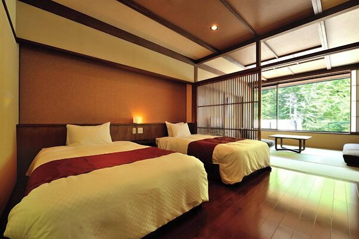 A hotel room with two beds, a window with a view of greenery, and a wooden floor.