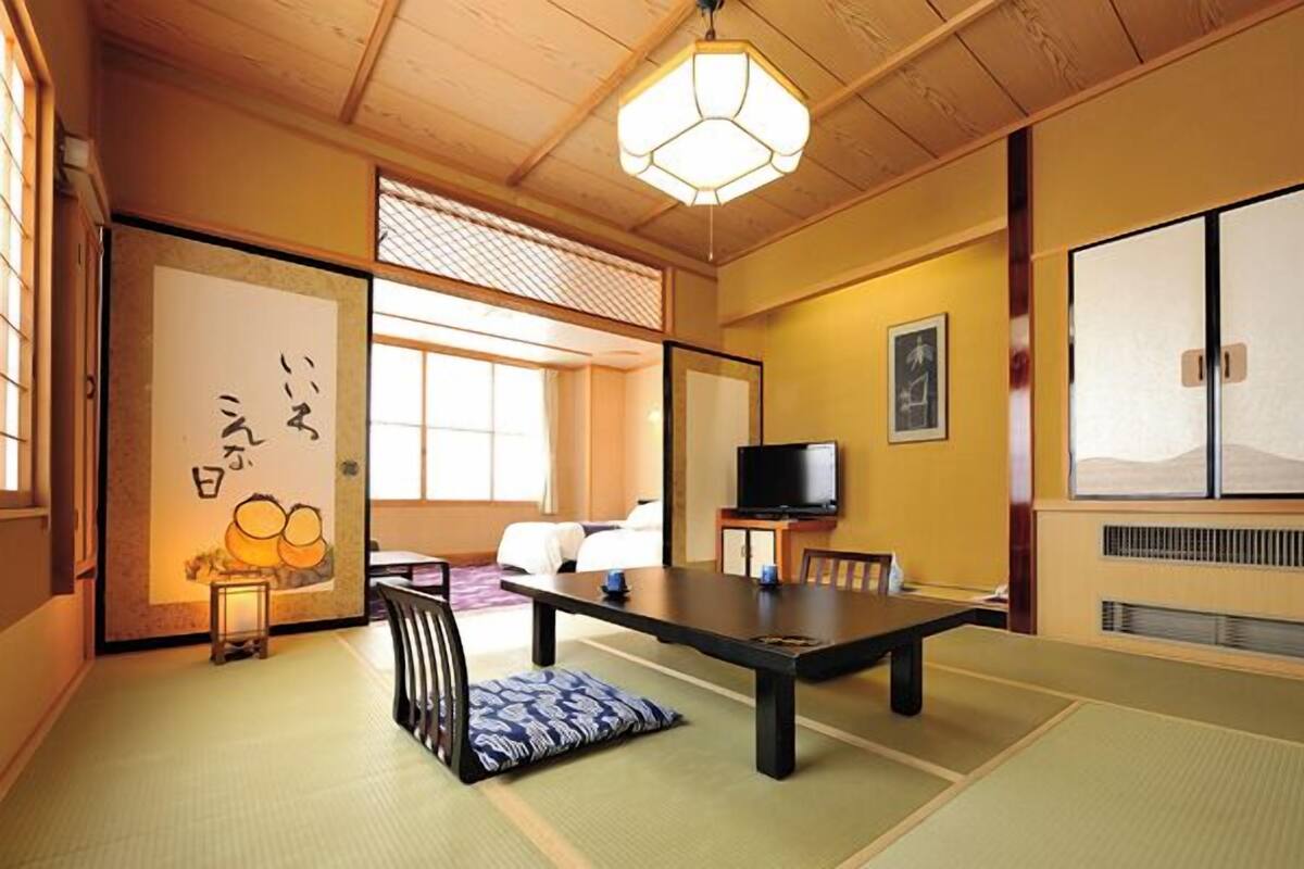A traditional Japanese room with tatami flooring, a low table, a television, and a sliding door.