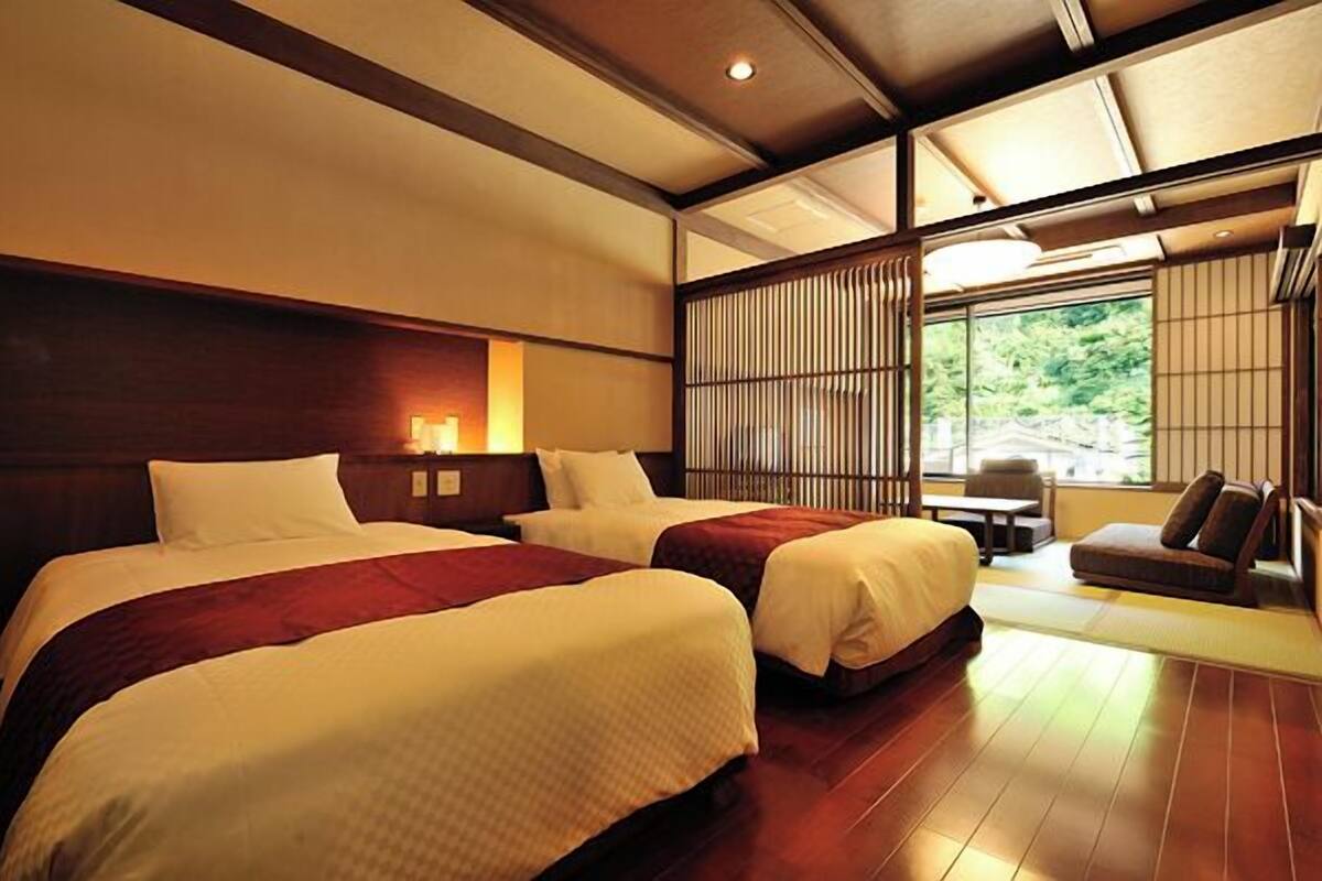 A hotel room with two beds, a seating area, and a view through a shoji screen.