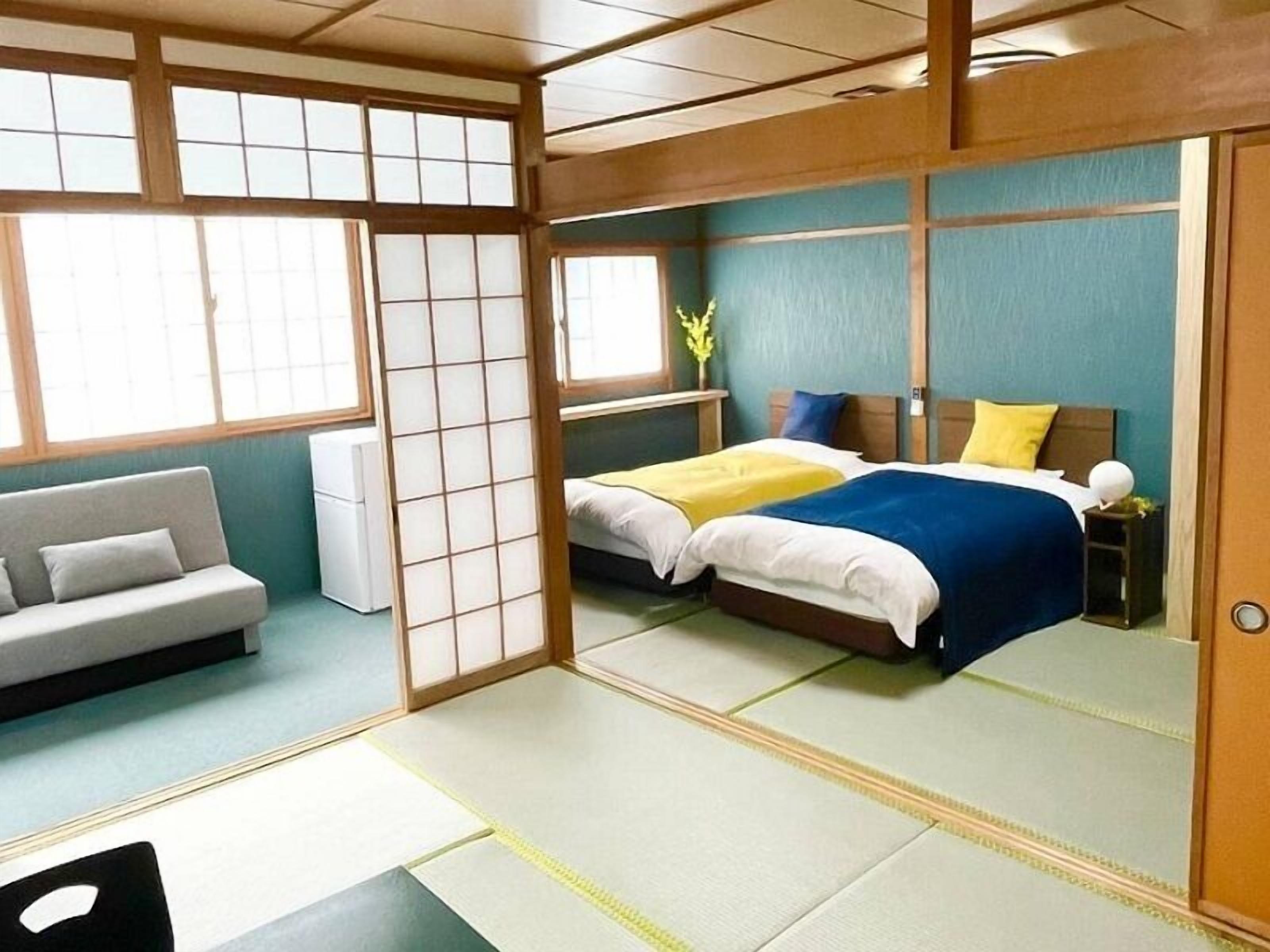 A traditional Japanese-style room with tatami flooring, a futon bed, a low wooden desk, and a sliding shoji screen.