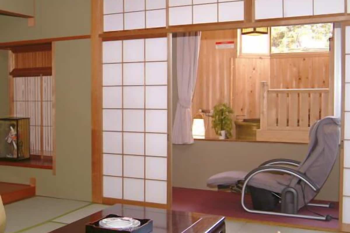 Una habitación tradicional japonesa con suelo de tatami, una mesa baja, una silla y puertas correderas.