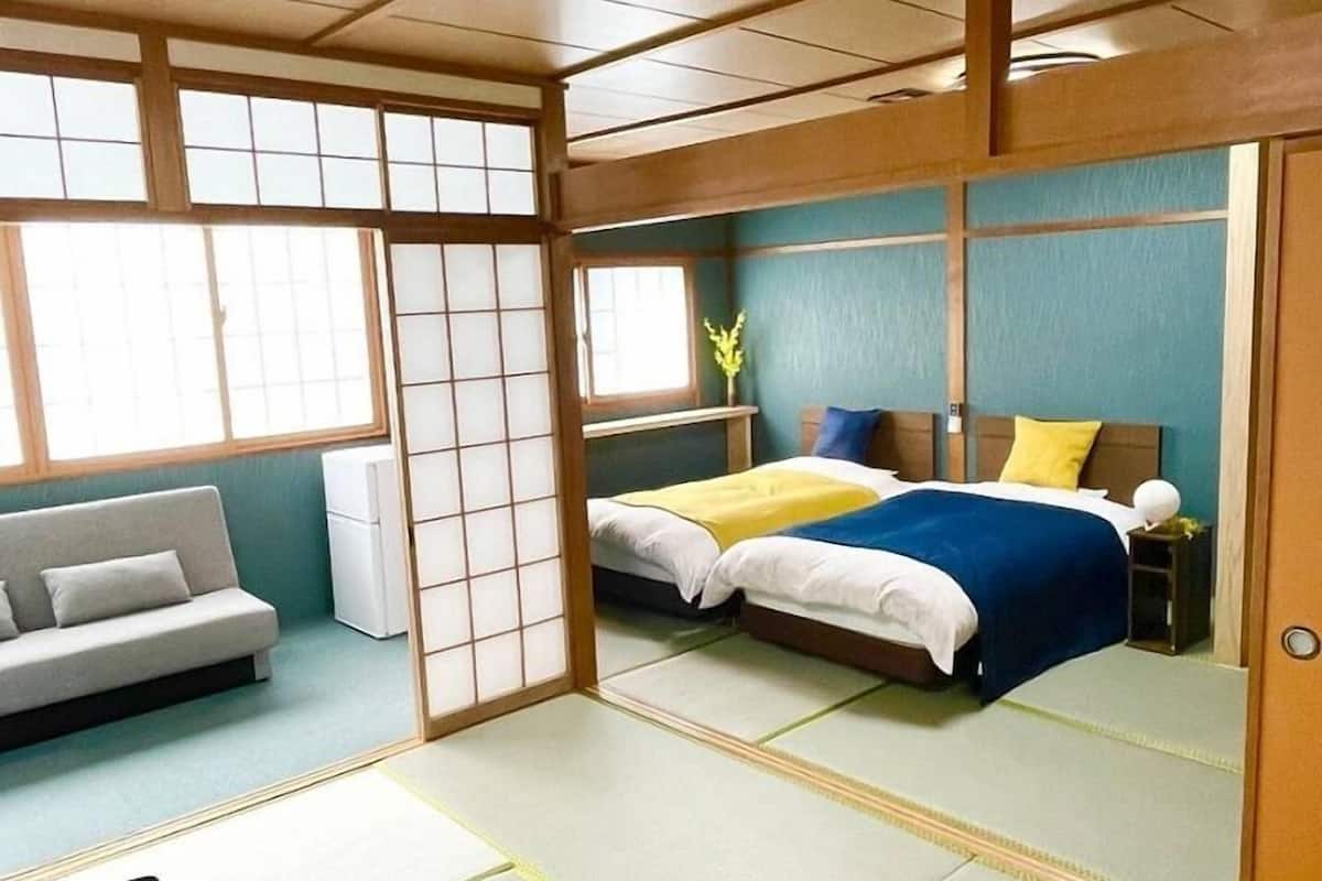 Una habitación tradicional japonesa con suelo de tatami, una cama con ropa de cama azul y blanca, un sofá y una ventana con vistas.