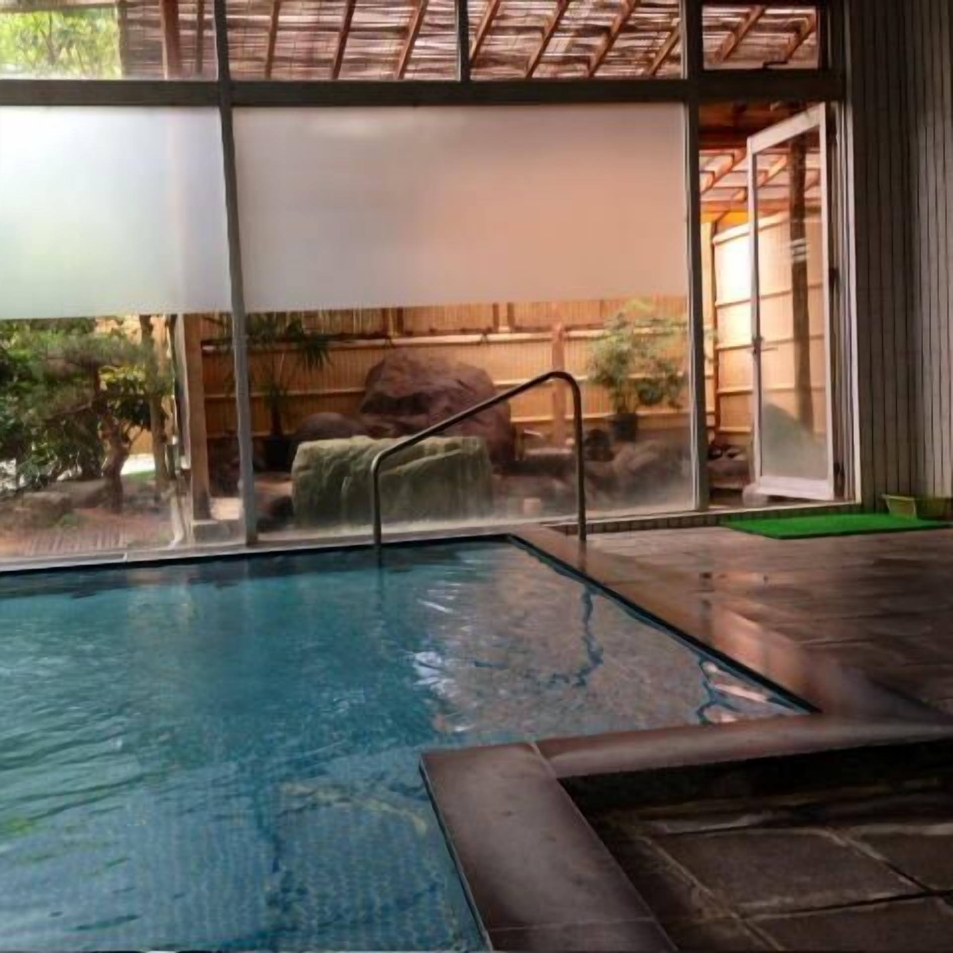 An indoor swimming pool with clear glass walls, a stone edge, and a metal ladder.
