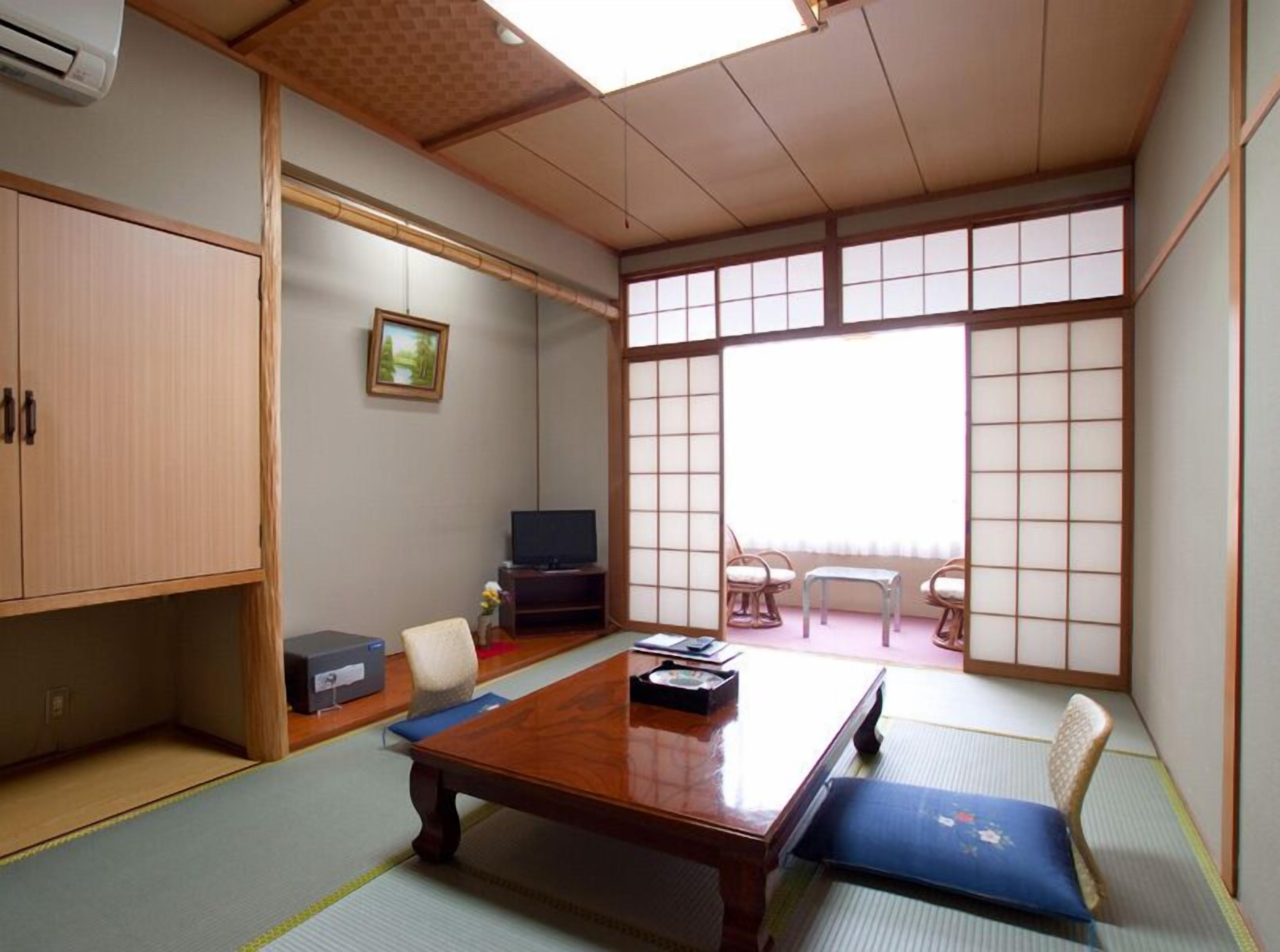 A traditional Japanese room with tatami flooring, a low wooden table, a television, and sliding doors.
