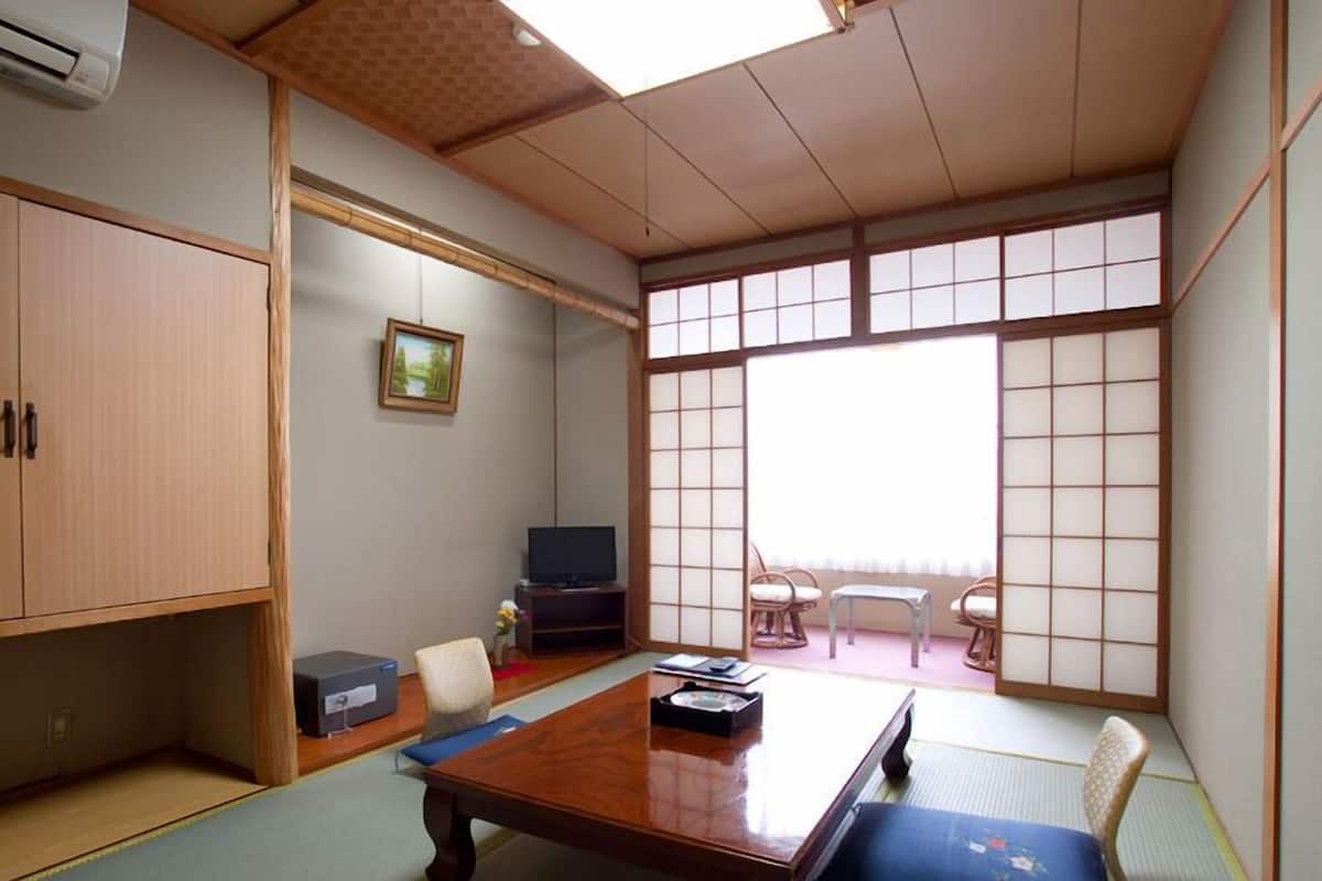 Una habitación tradicional japonesa con suelo de tatami, una mesa de madera baja, un televisor y puertas correderas.