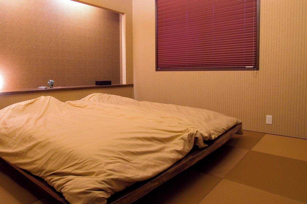 Una habitación de hotel con cama, mesita de noche, espejo y ventana con persianas.
