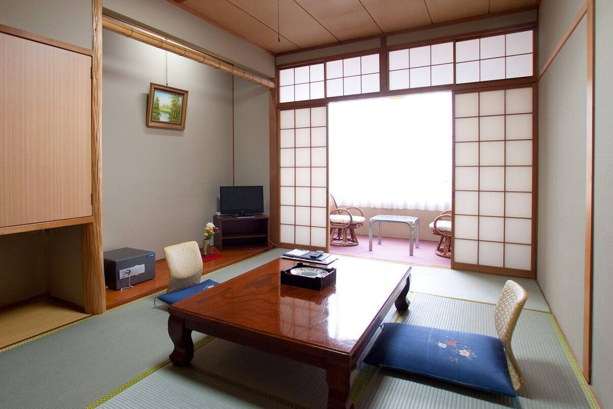 Una habitación japonesa tradicional con suelo de tatami, una mesa baja, un televisor y puertas correderas.