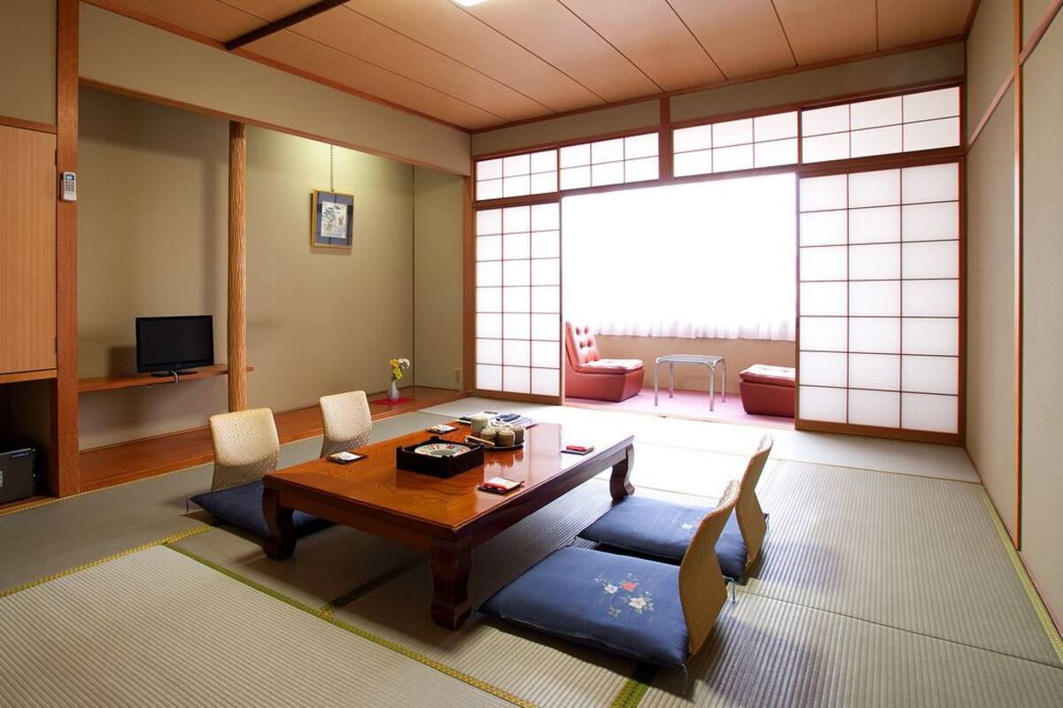 Una habitación japonesa tradicional con suelo de tatami, una mesa de madera baja y un puertas correderas que dan a un balcón.