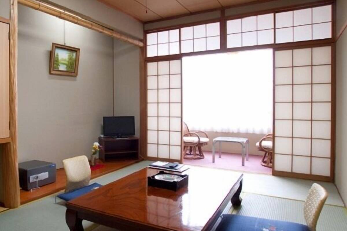 Una habitación tradicional japonesa con suelo de tatami, una mesa de madera baja, un televisor y puertas correderas shoji.