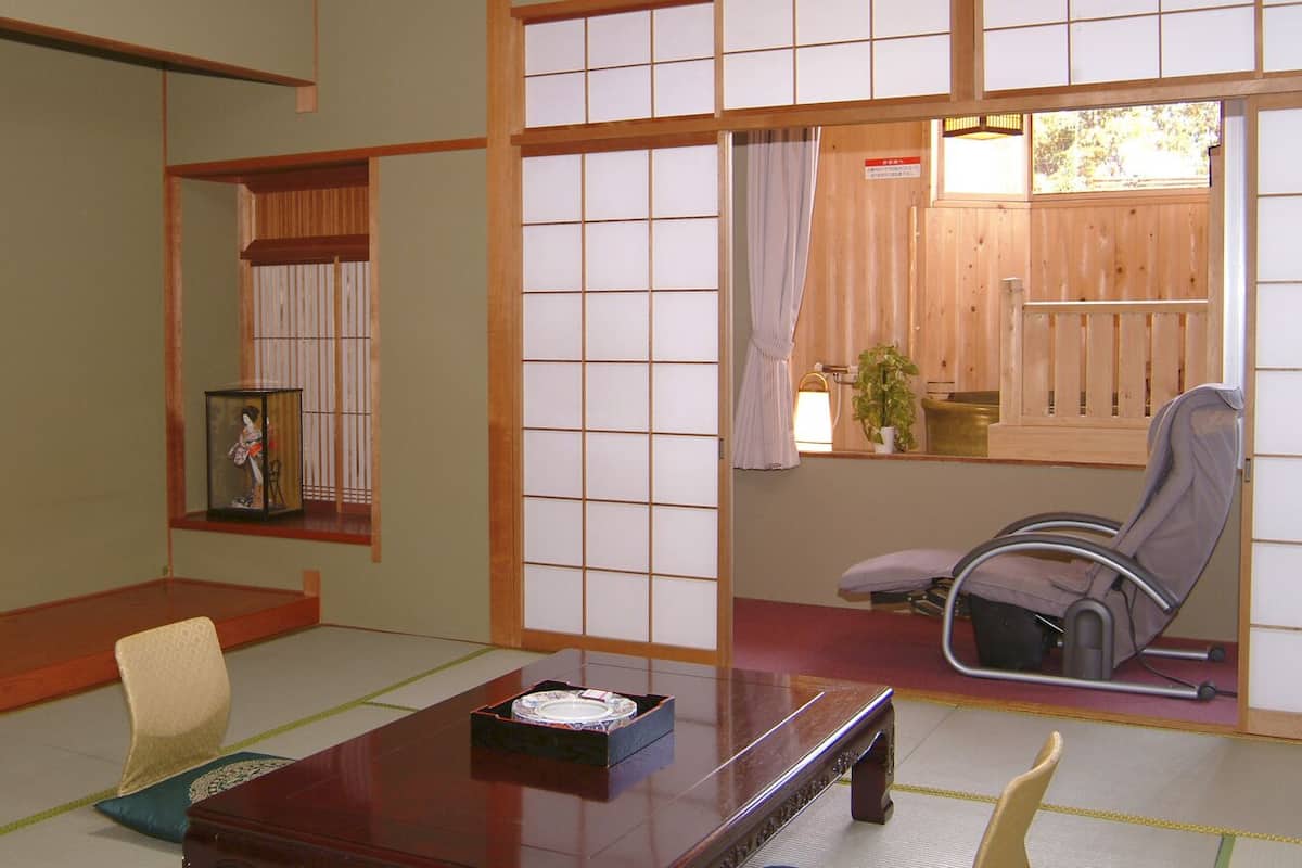 Una habitación japonesa tradicional con suelo de tatami, una mesa baja, una silla y una puerta corrediza que da a un balcón.