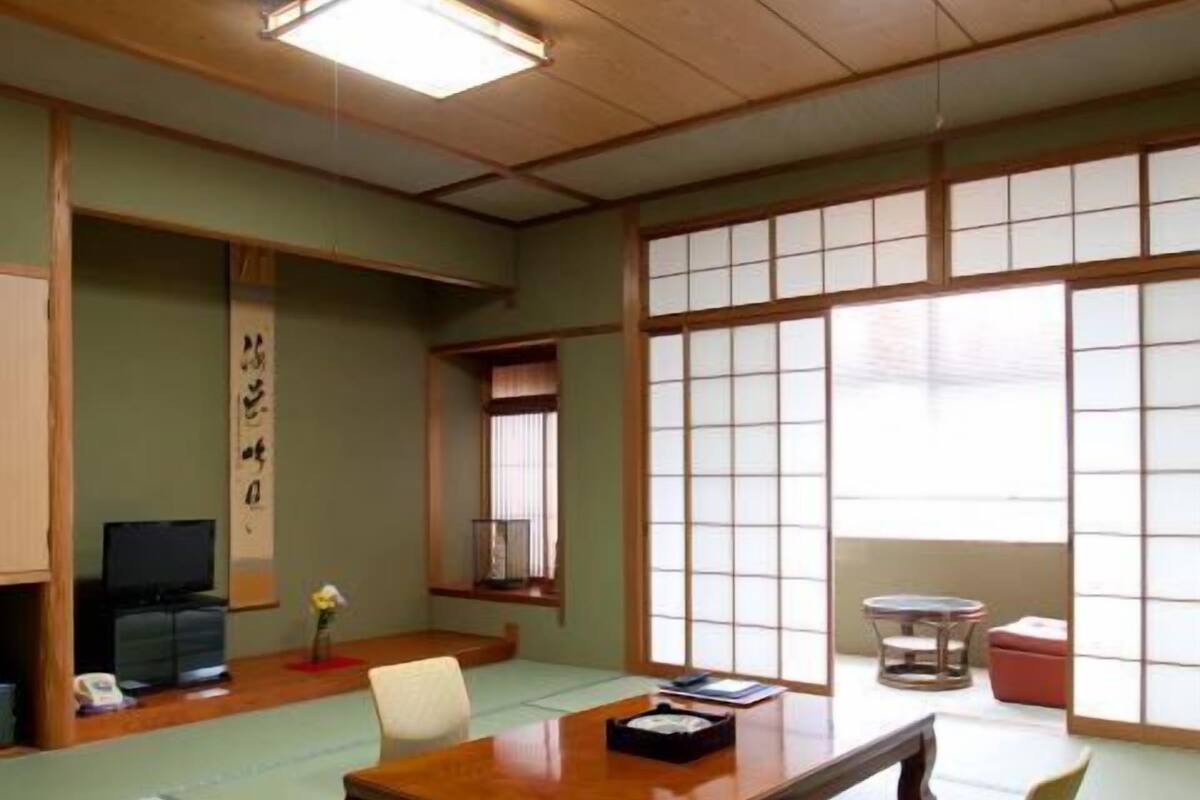 Una habitación japonesa tradicional con suelo de tatami, una mesa de madera baja, un televisor y puertas correderas shoji.