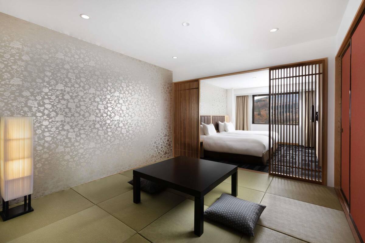 Habitación de hotel con suelo de tatami, cama con vistas, una mesa y puerta corredera tradicional.