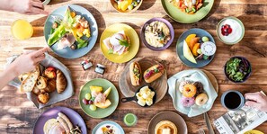 Variedad de productos para el desayuno, como pasteles, frutas y bebidas, sobre una mesa de madera.