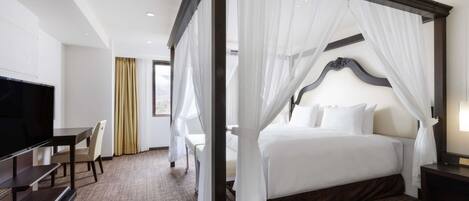 Habitación de hotel con cama con dosel, televisión, escritorio y vistas al exterior.