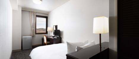 A hotel room with a bed, a desk with a chair, a television, a lamp, and a window with curtains.
