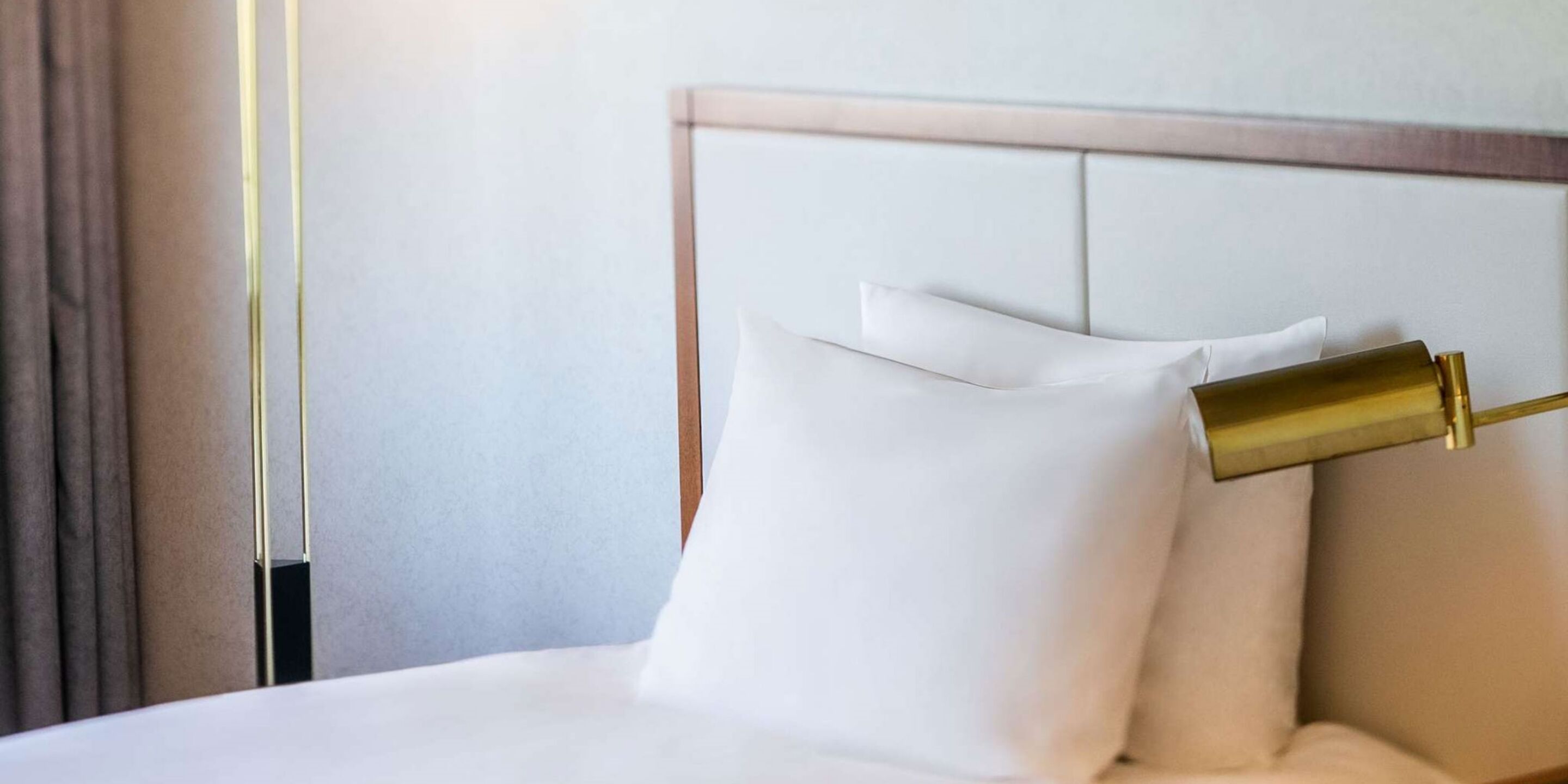 A neatly made bed with white linens and a gold-colored headboard.