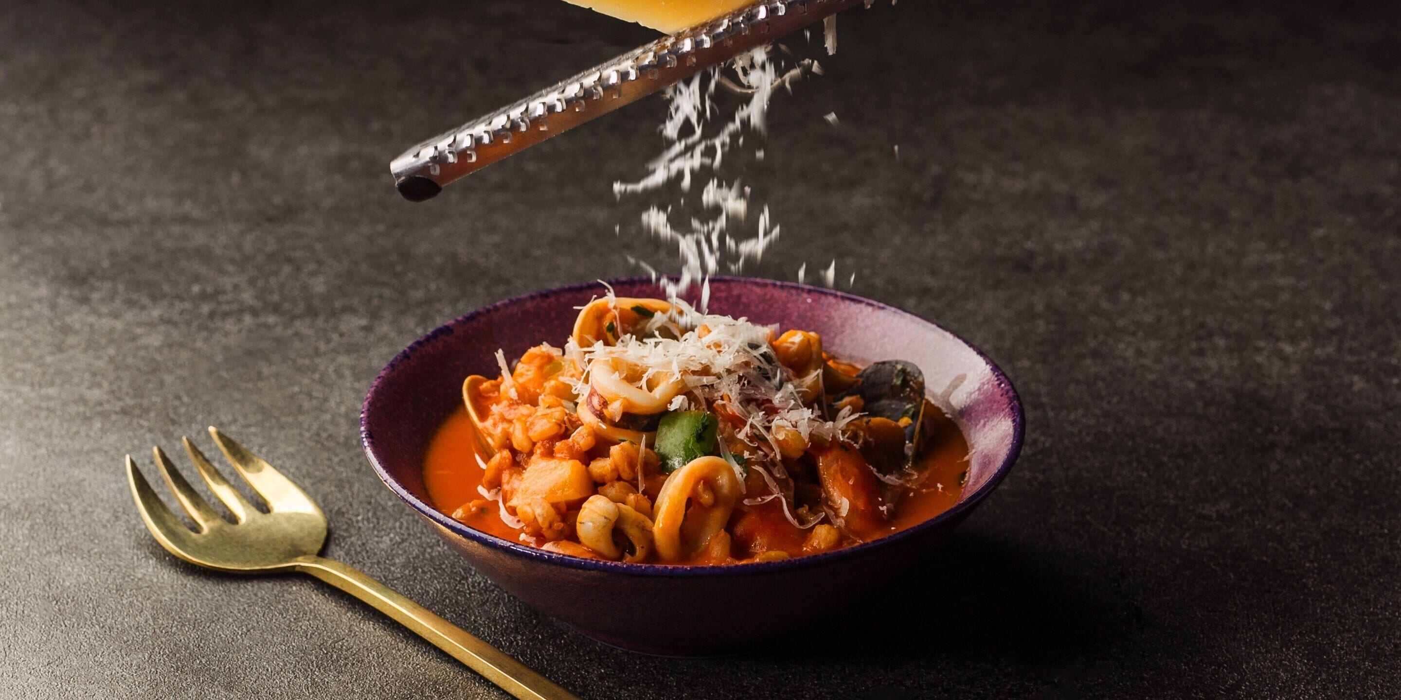 A bowl of pasta with cheese and a fork beside it.