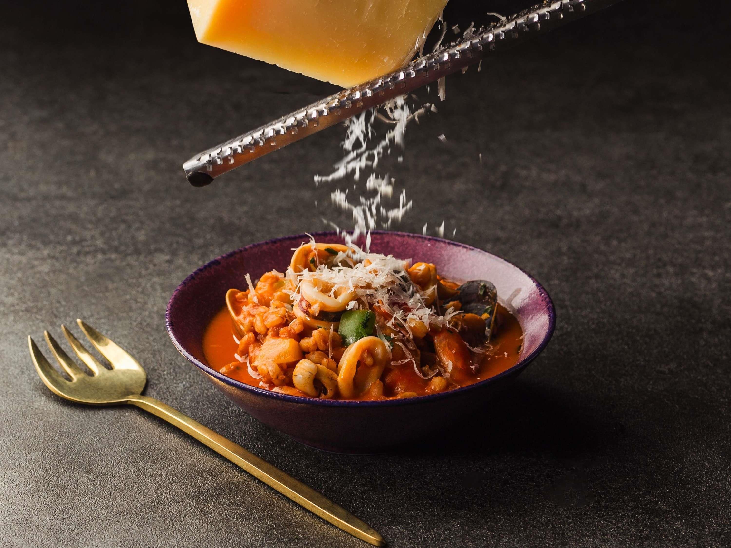 A bowl of pasta with cheese and a fork beside it.