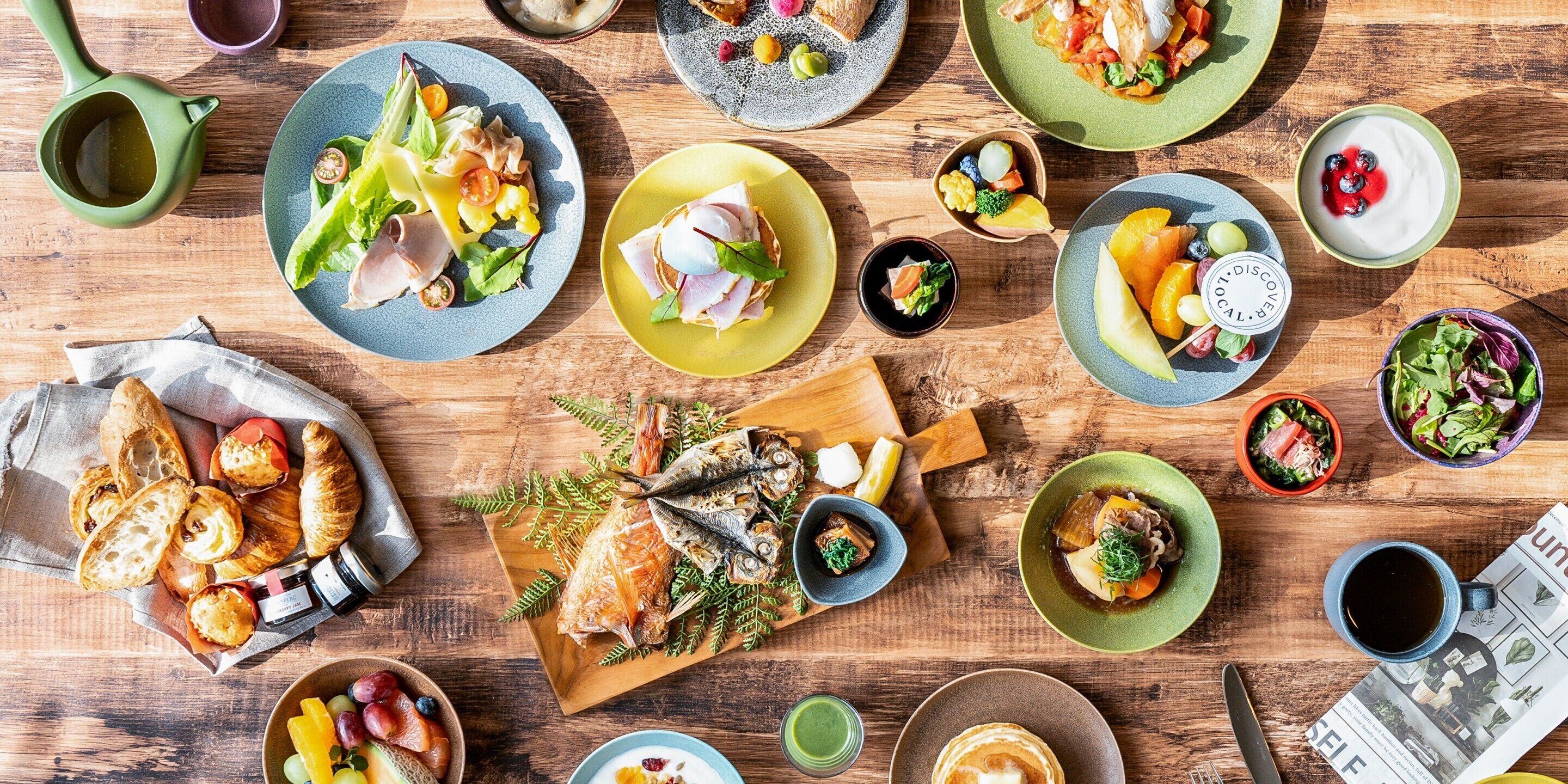 Verschiedene Speisen und Gerichte auf einem Holztisch, darunter Fisch, Salate und Gebäck.