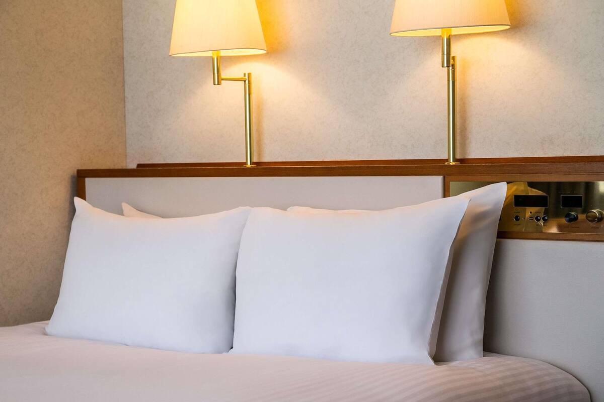 Una habitación de hotel con una cama, dos lámparas de noche y un panel de control en la pared.