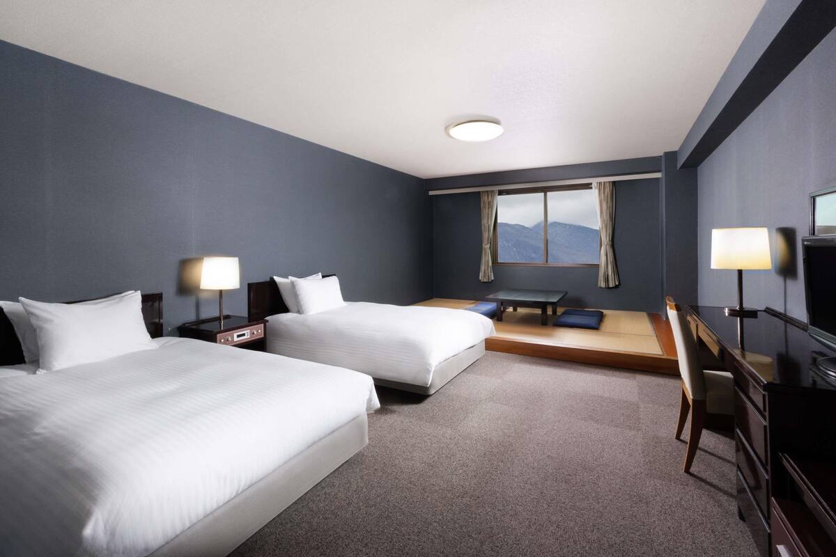 Habitación de hotel con dos camas, un escritorio, una silla, un televisor y una ventana con vistas a la montaña.