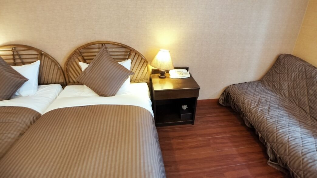 A hotel room with two beds, a nightstand with a lamp, and a small table.